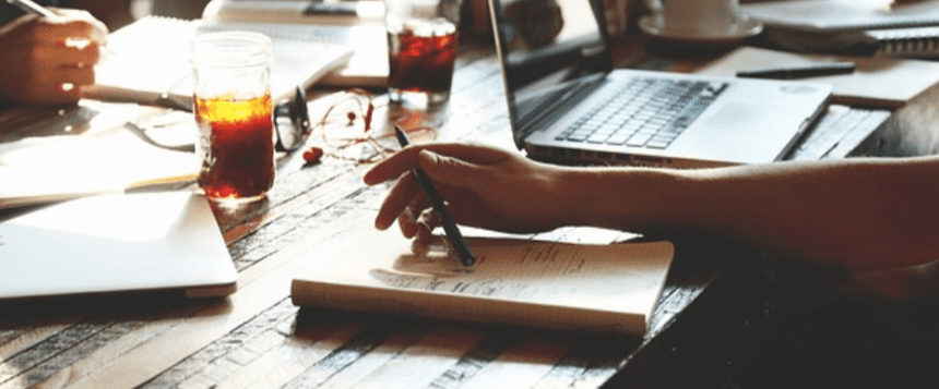 Person writing in a notebook with a laptop nearby.
