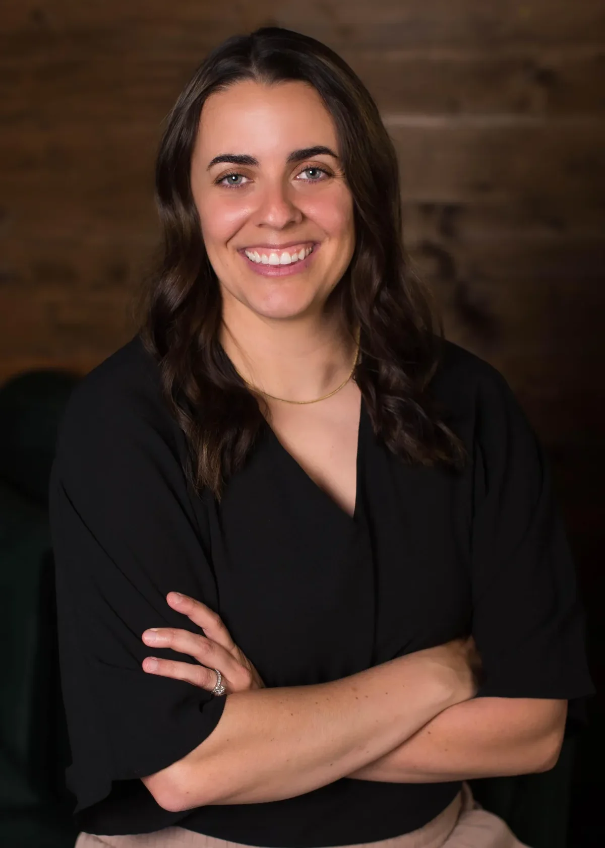 Smiling person with crossed arms, wood background.